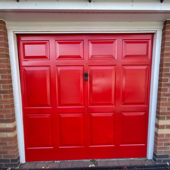 Red garage door with a black handle in the center, framed by brick walls.