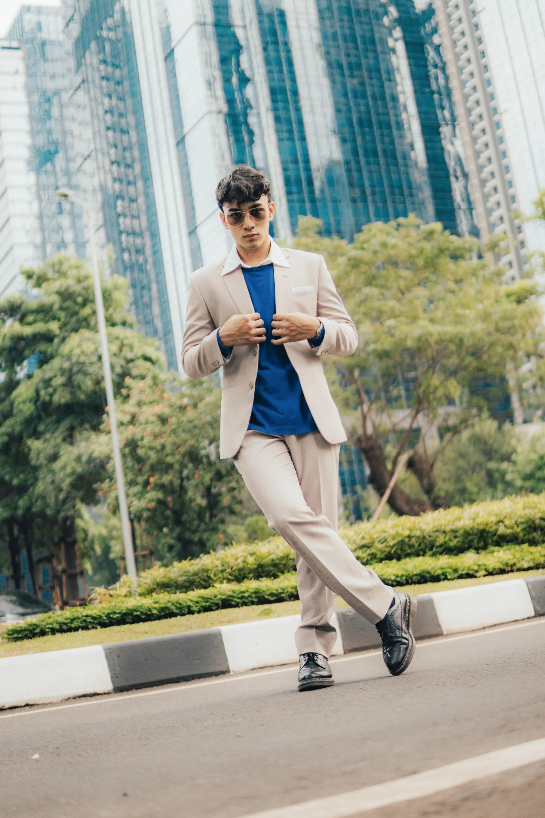 Man in beige suit and blue shirt posing on city street with skyscrapers in background