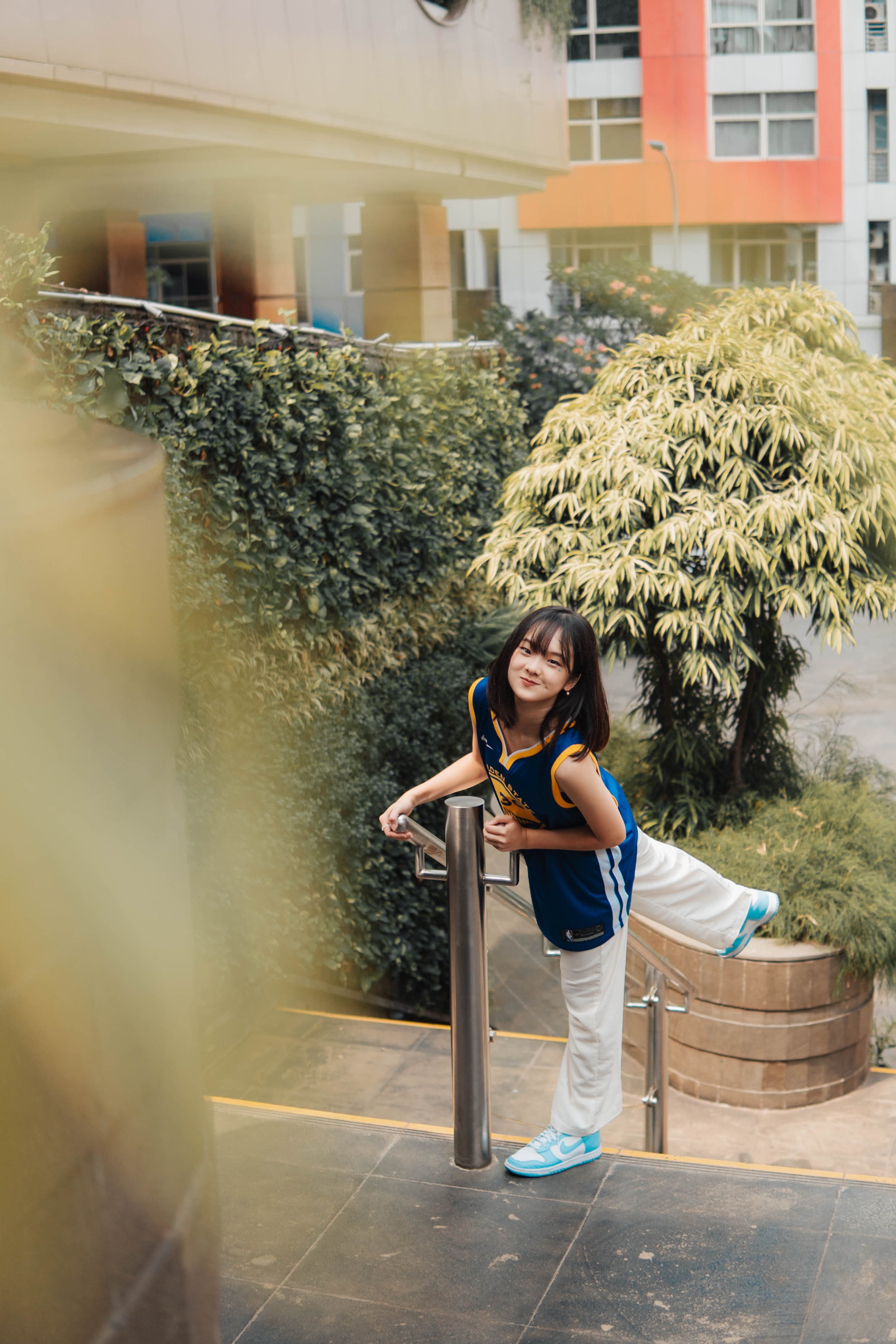 Woman in athletic outfit stretching by railing in urban garden environment.