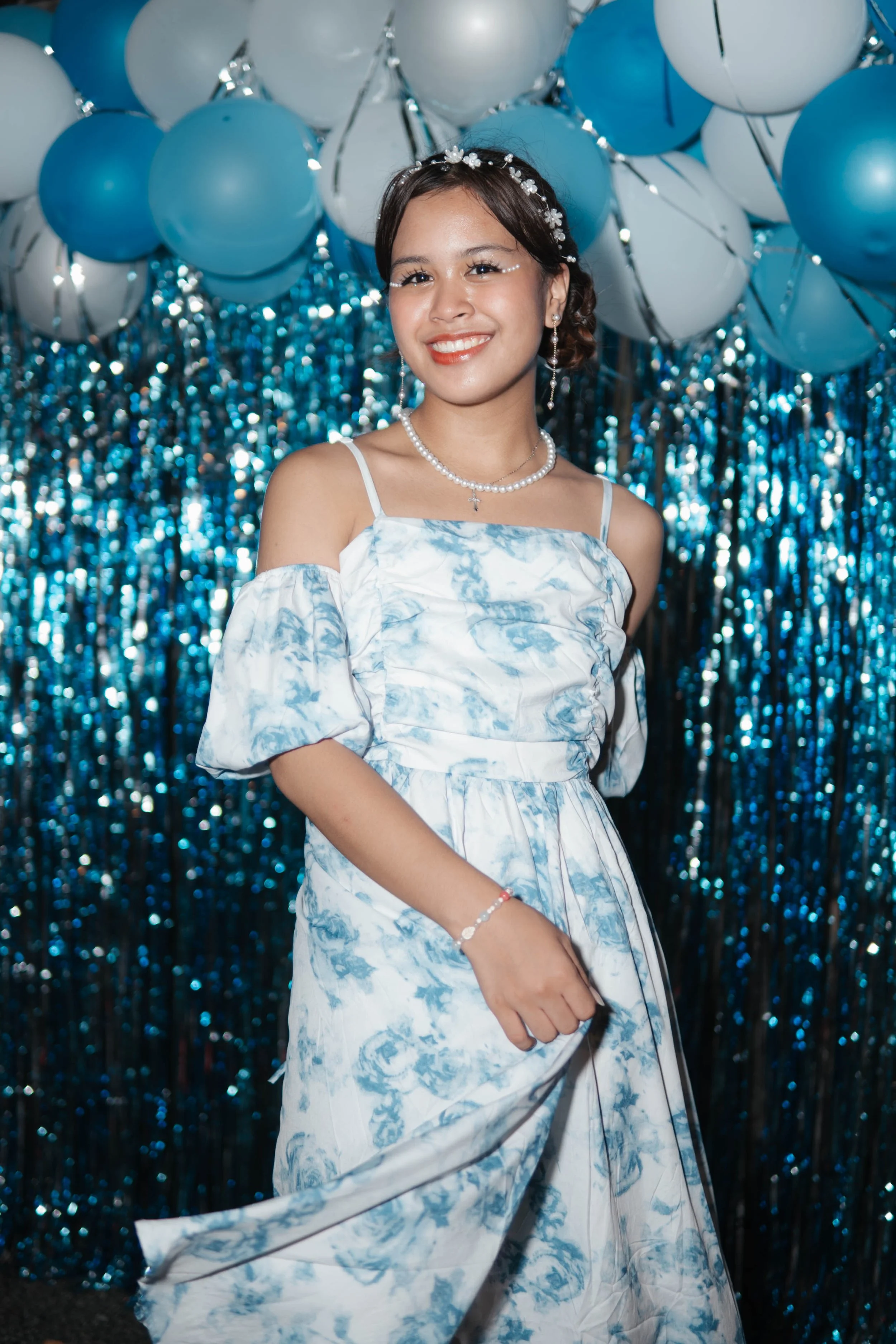 Girl in floral dress at party with blue balloons and tinsel backdrop.