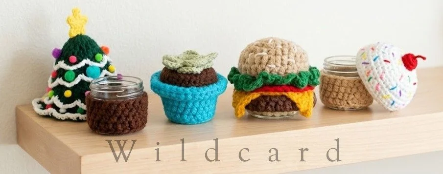 A decorated wooden shelf displaying various items including a small knitted Christmas tree, two glass jars with crochet covers, a knitted cupcake, a crocheted hamburger, and a crocheted heart with rainbow sprinkles and a cherry on top.