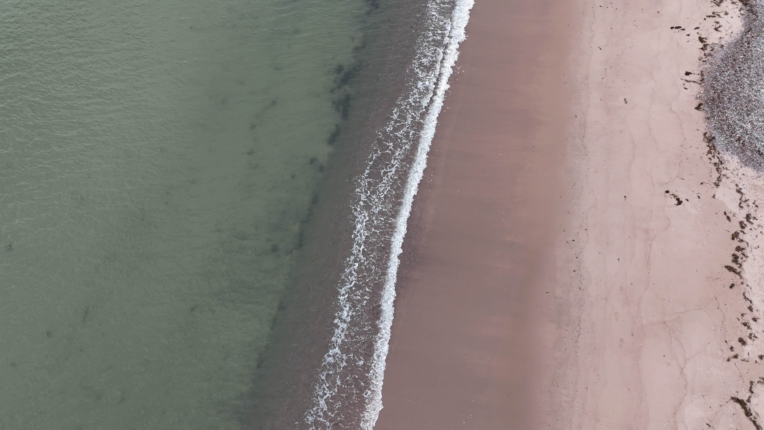 Aerial view of a beach showing gentle waves hitting the sandy shore.