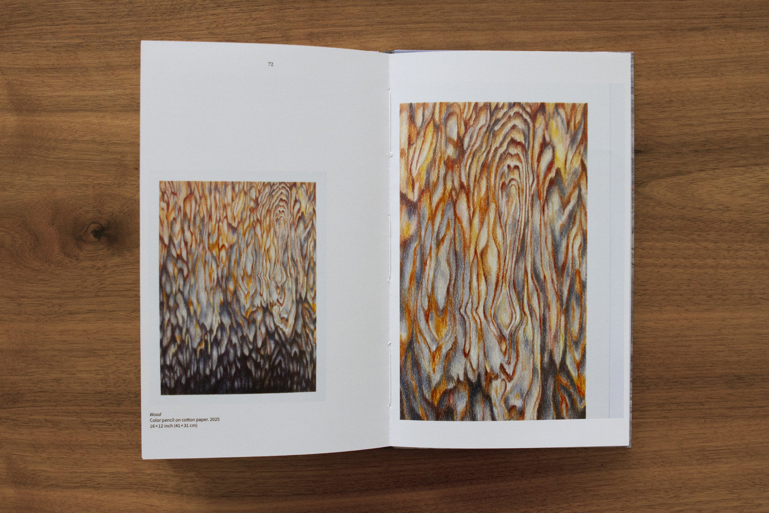 Open booklet on wooden surface showing abstract artwork resembling wood grain, with text indicating artwork titled "Wood" made with colored pencil on cotton paper, 16x12 inches. Dibujos, espuma, agua, textura naturaleza. Arte gráfico. Galeria NAc.