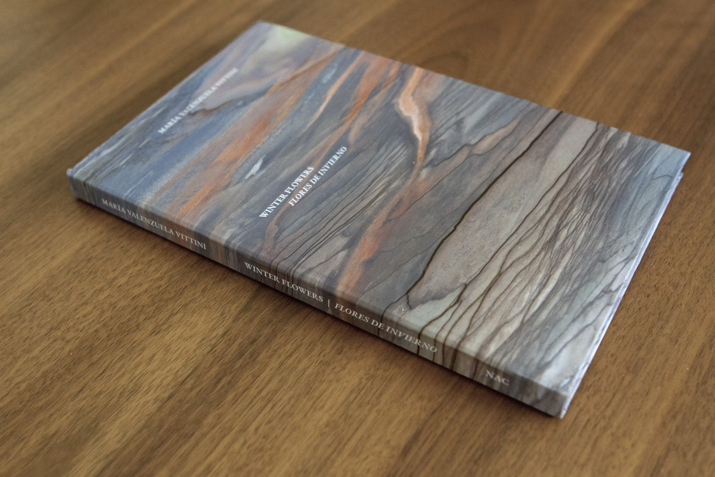 A book titled "Winter Flowers" by Mariana Valenzuela Vittini lying on a wooden surface.