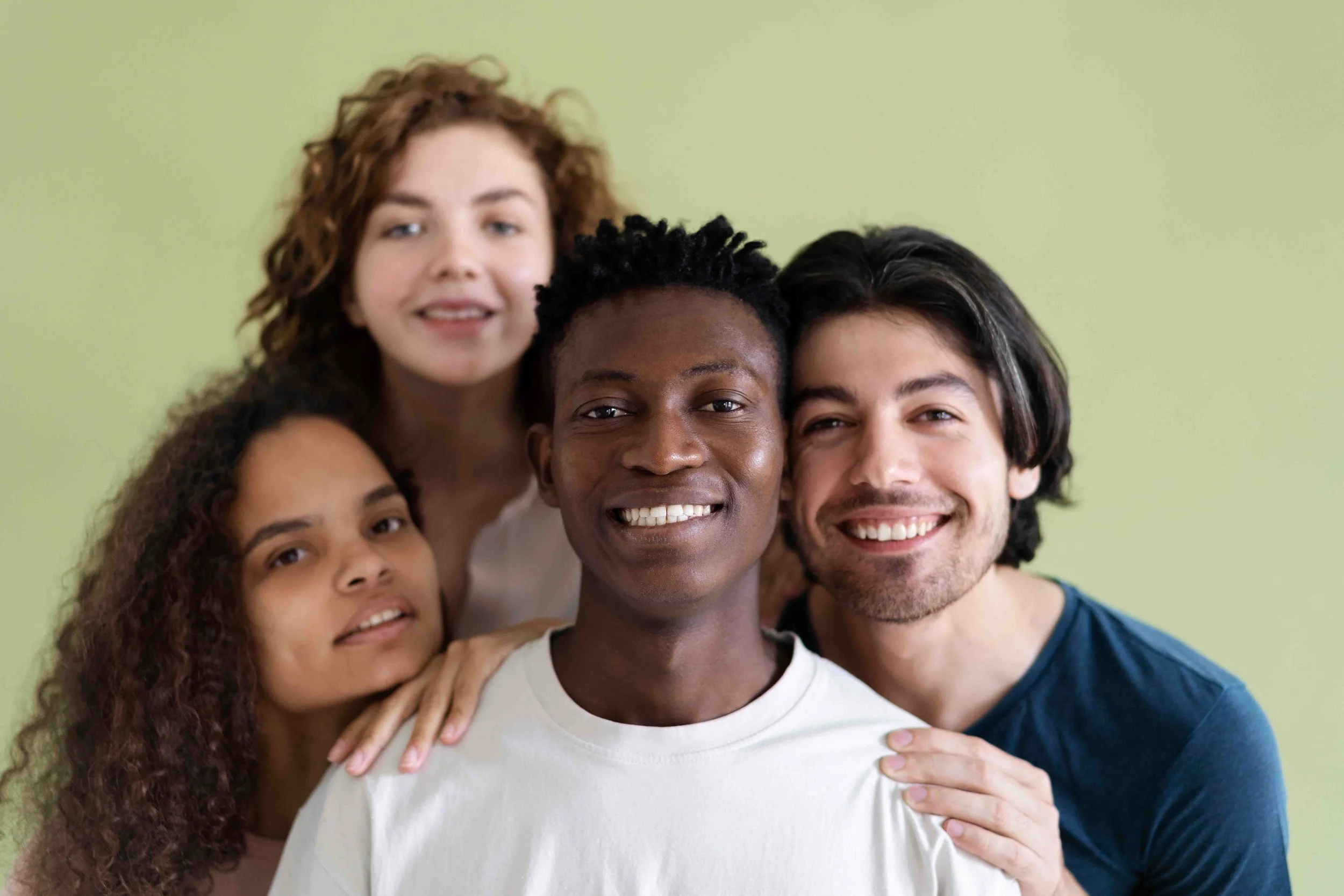 Group of five diverse young adults smiling and posing together against a light green background.