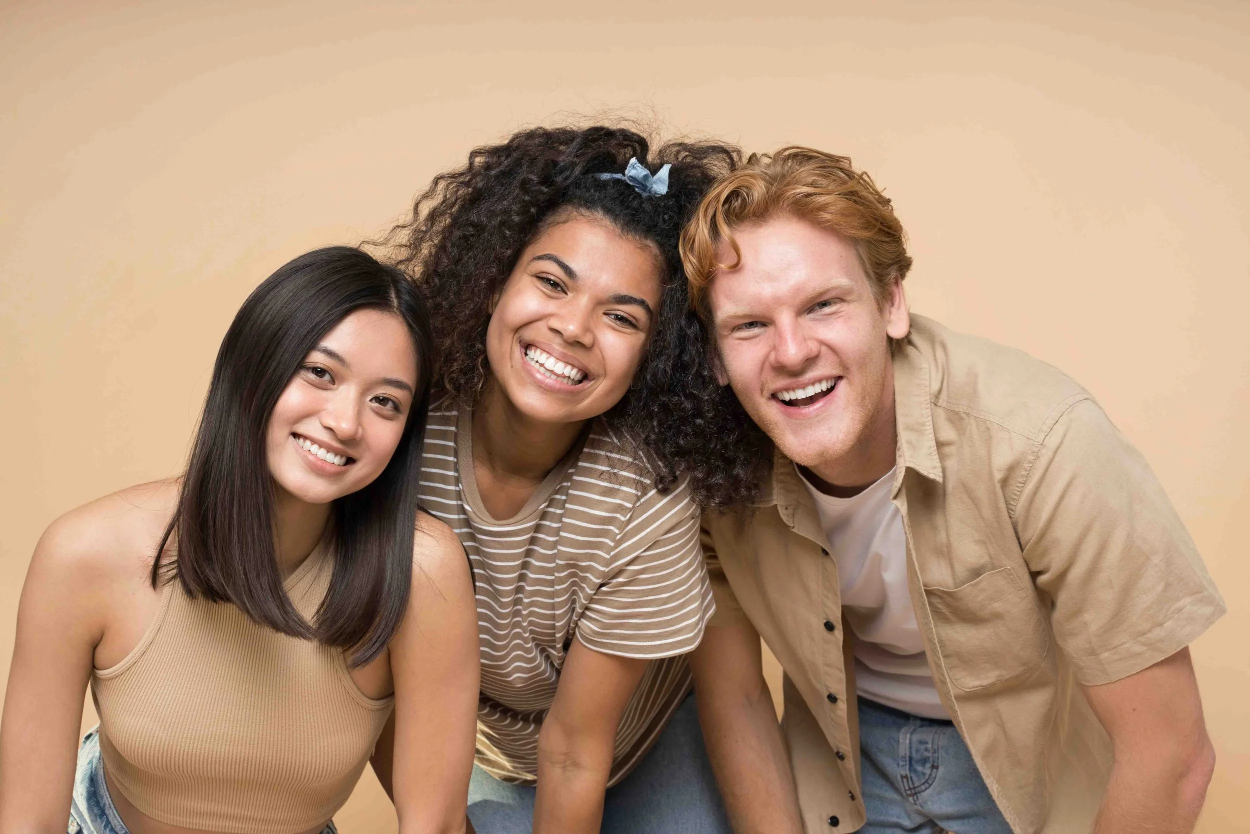 Three young adults smiling close together against a beige background.