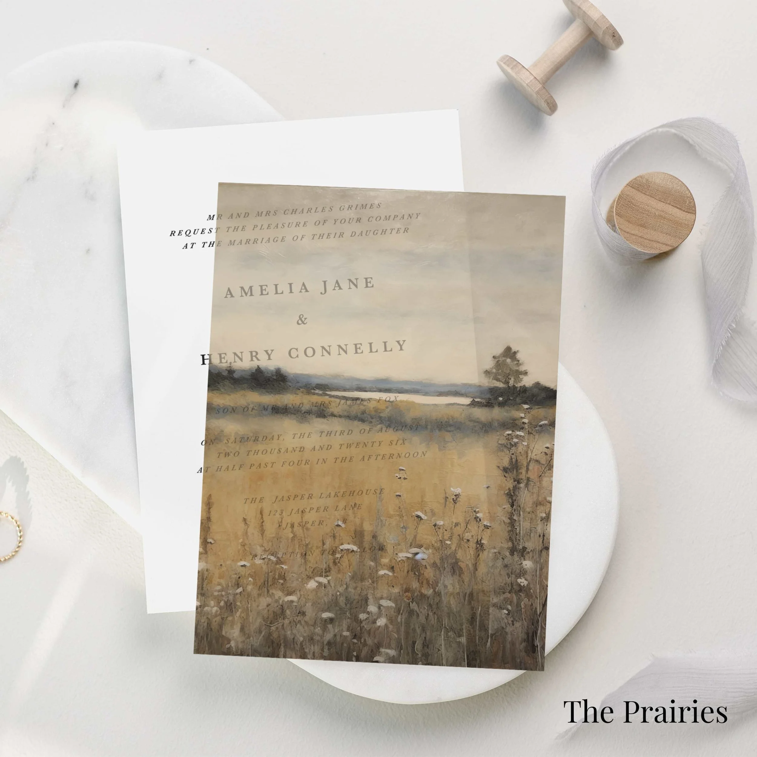 Wedding invitation featuring a landscape painting of prairies, with text details overlaying the image. The background is white with minimal decor, including a wooden spool and a ribbon. The bottom right corner reads "The Prairies."