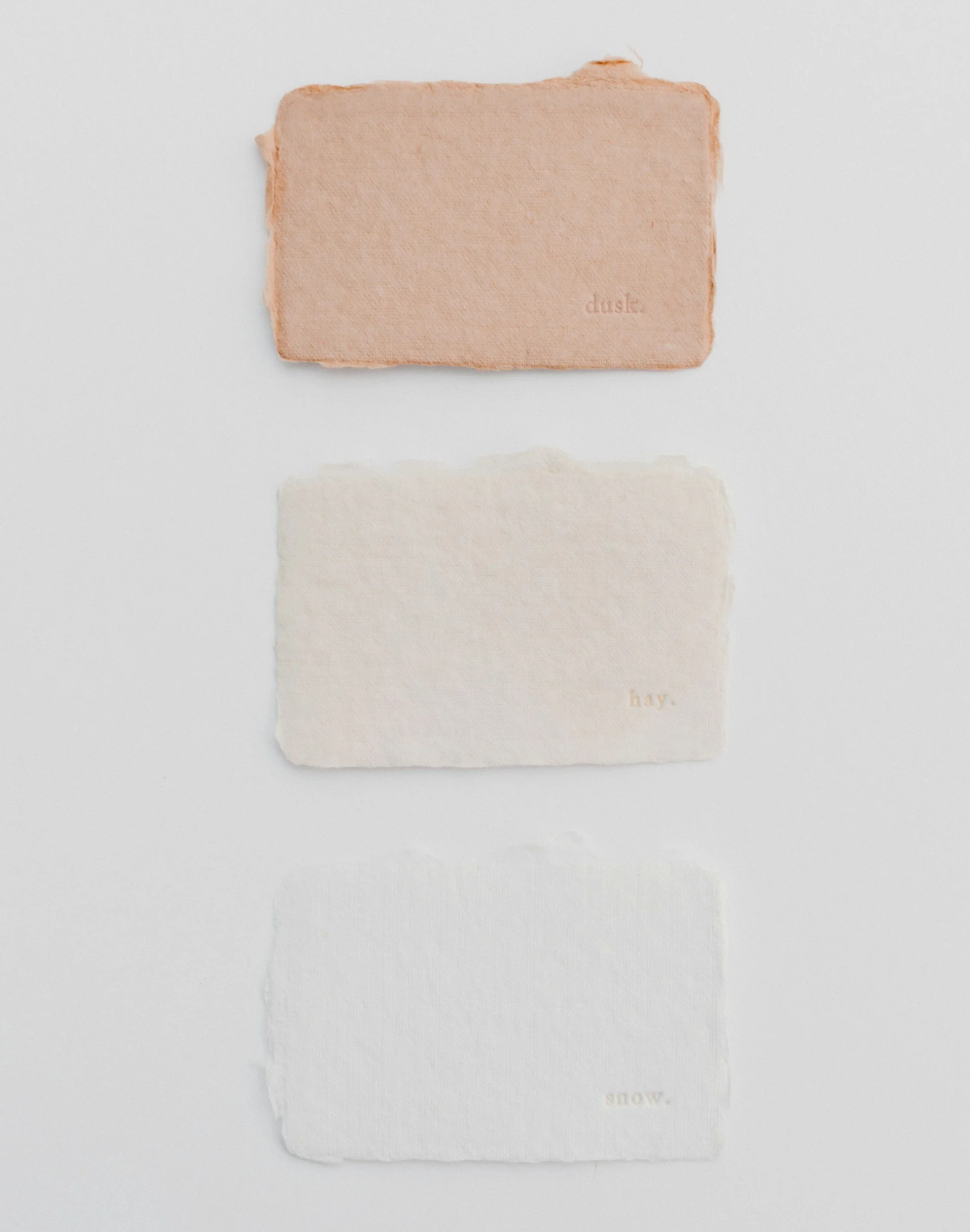 Three torn paper sheets with the words "dusk," "hay," and "snow" printed in small text at the bottom right corner, arranged vertically on a white background.