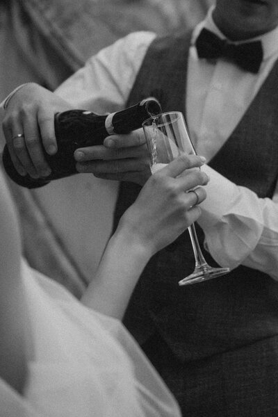 A person in formal attire pours champagne into another person's glass at a celebration or event.