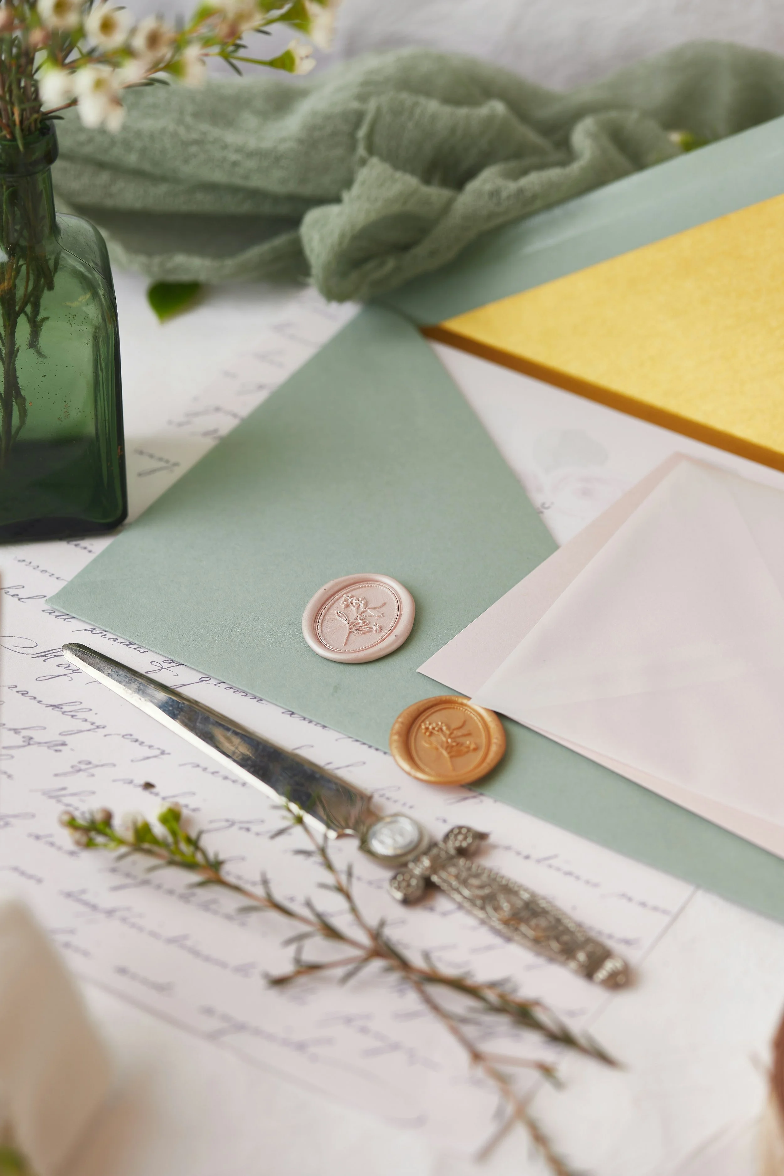 Decorative stationery and floral arrangement on a table, including colored paper, wax seals, a silver watch, and a vintage key.
