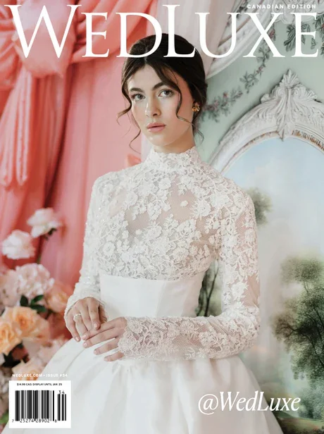 Cover of WedLuxe magazine featuring a woman in a white lace wedding gown with lace sleeves, standing in a room with pink curtains, flowers, and a mirror.