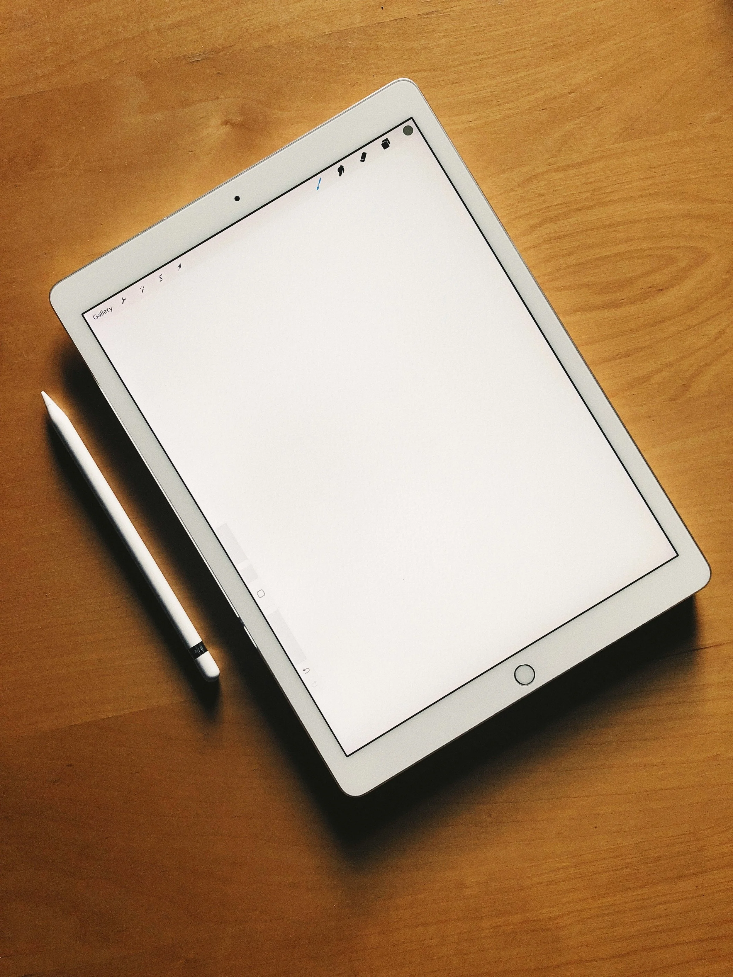 An iPad with a stylus placed on a wooden table, displaying a blank white page.