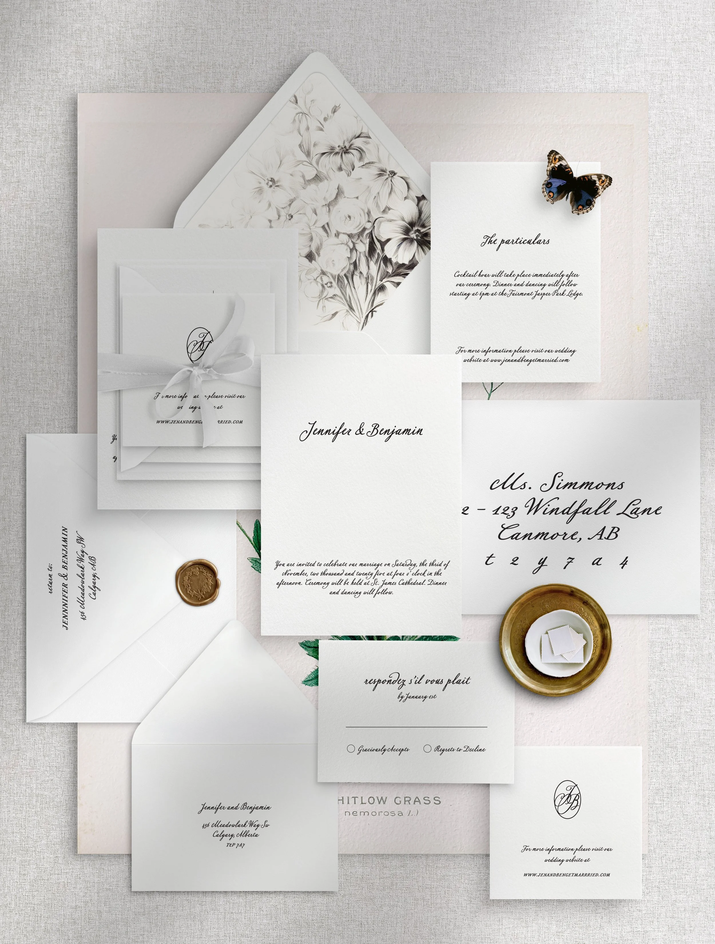 Wedding invitation suite with white and black floral design, RSVP card, envelope with gold seal, and decorative butterfly, arranged on a light-colored fabric background.
