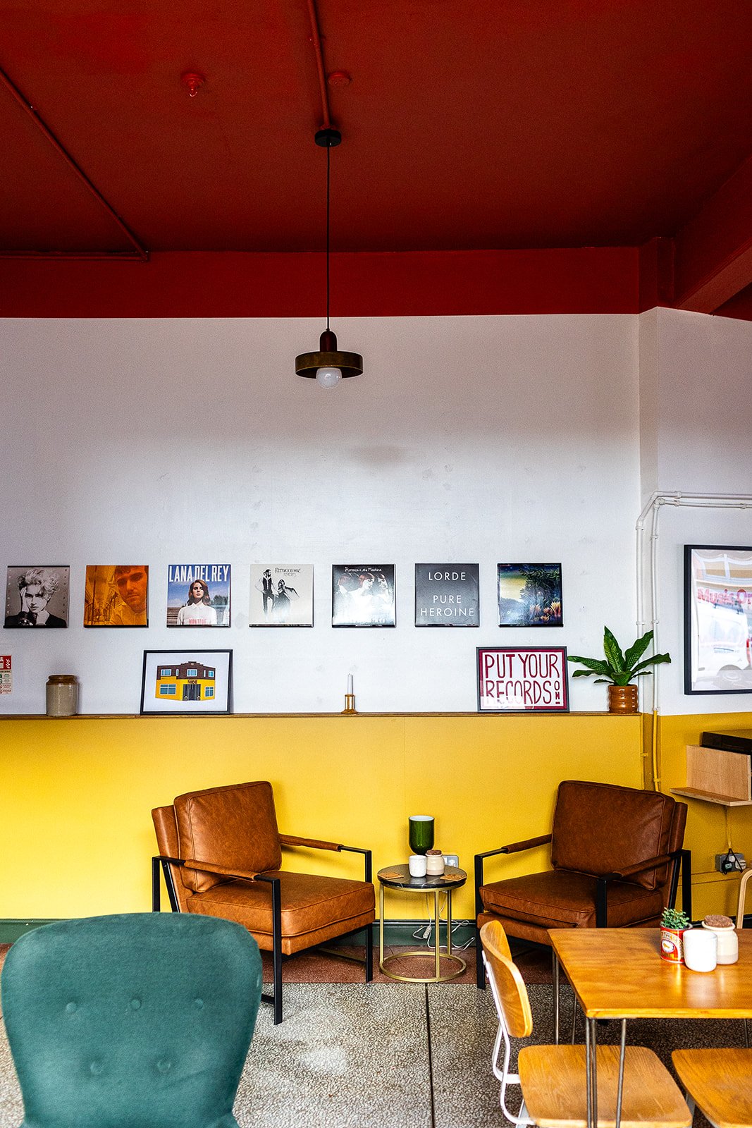 Image of the Front Room space at The Hide wedding and events venue, Sheffield. Mustard wall half way up and the top half white. Records are deployed on the walls and below two brown leather lounge chairs withe a side table. 