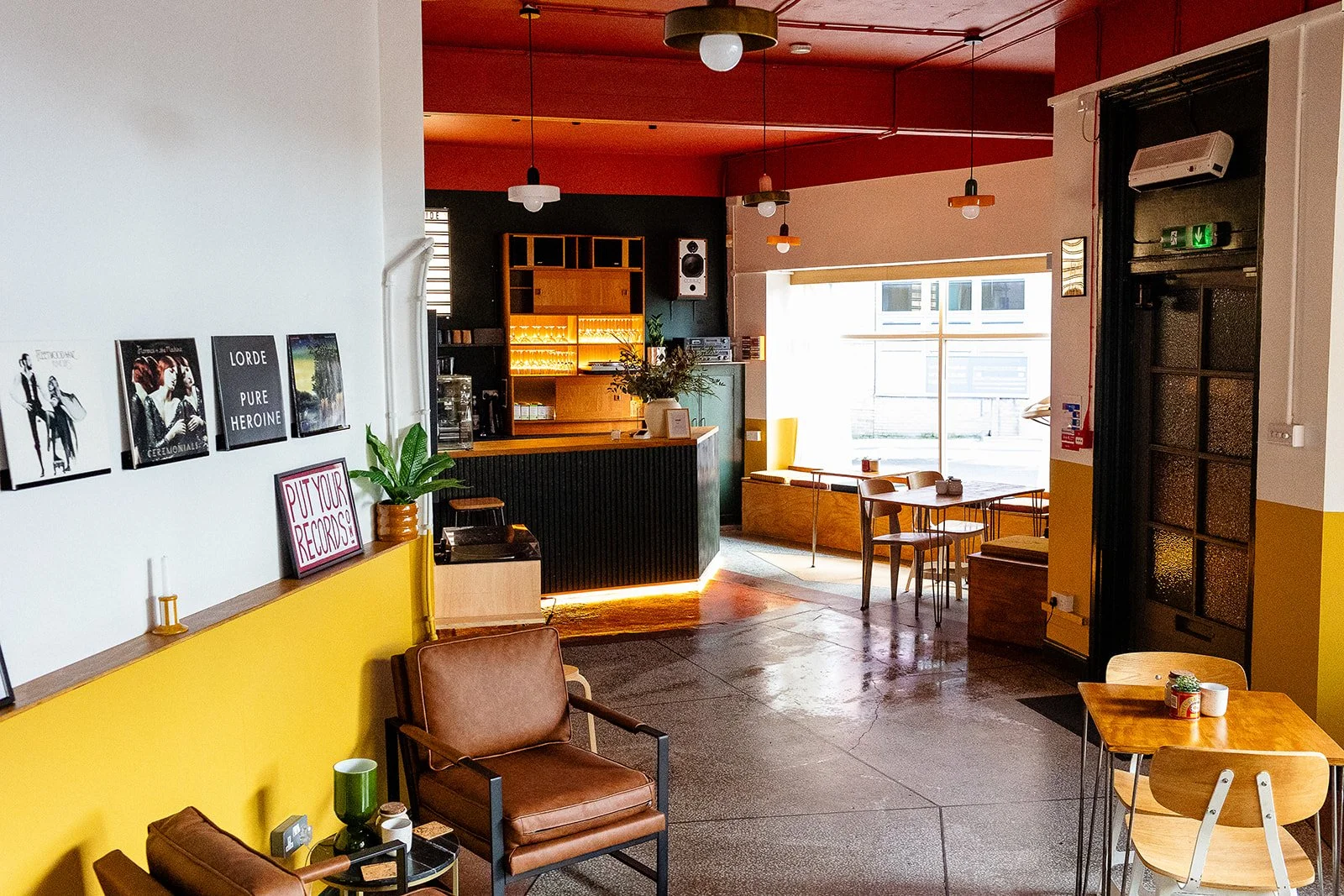 Welcome entrance at The Hide, wedding and events venue, Sheffield. Image shows brown leather lounge chairs and a bar at the back. The room is decorated in white, mustard yellow, dark green and red colours.