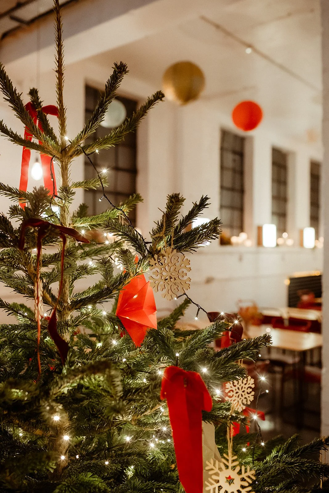 Decorated Christmas tree with red ribbons, paper ornaments, and white lights in a cozy room with candles and festive decorations.