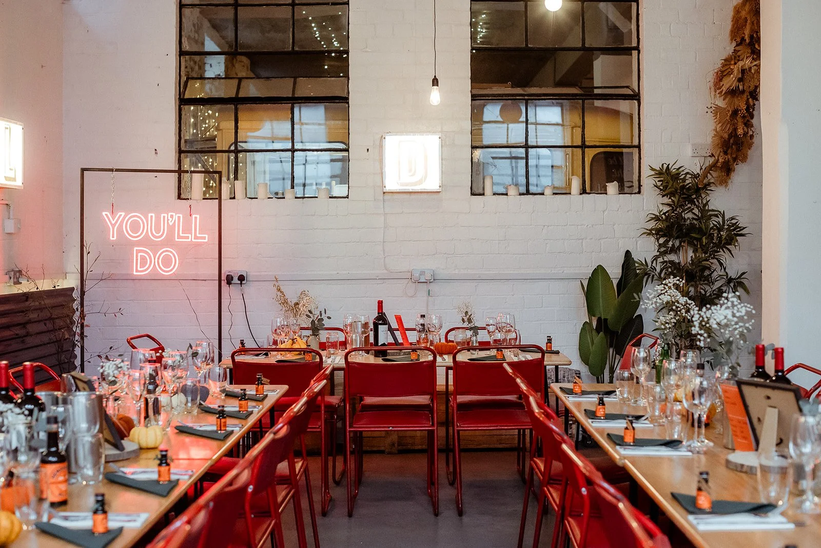 Canteen warehouse at The Hide showing tables set for a wedding with original reclaimed red cox chairs. Tables decorated with flowers and candles.