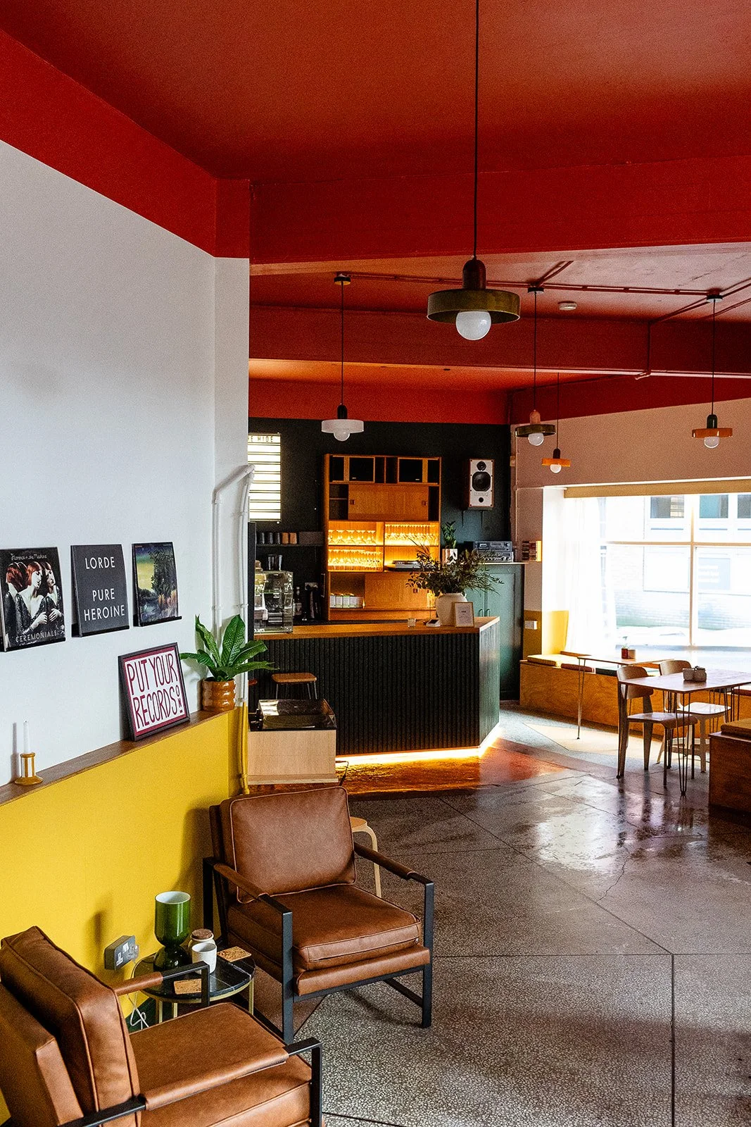 Front Room at The Hide. The welcome space at weddings and events. decorated with a red ceiling, and white and mustard walls. The image shows two lounge chairs and a green bar in the background. 