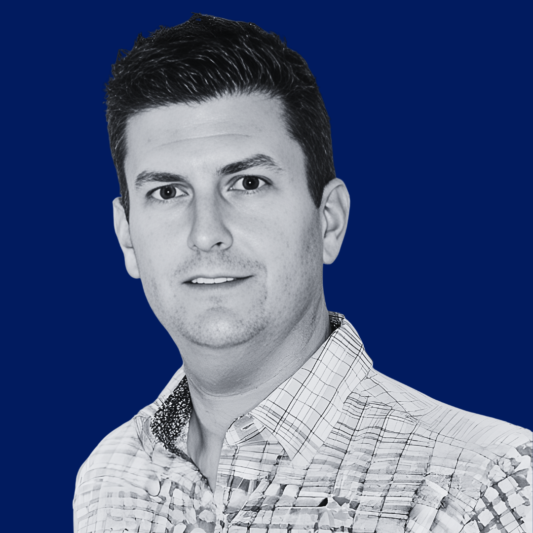 Black and white portrait of a man with dark hair, wearing a checked shirt, against a solid blue background.