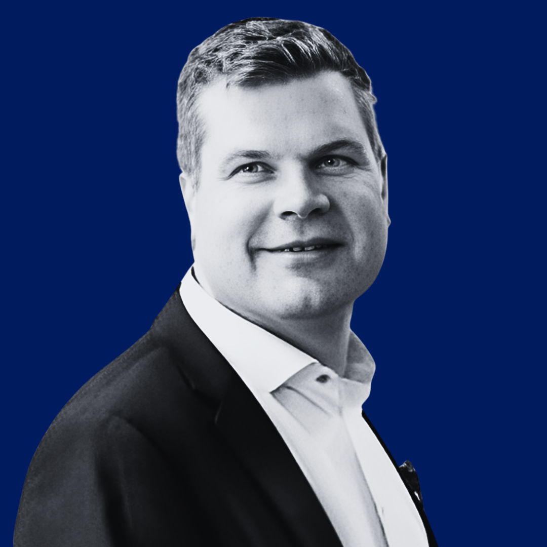 Black and white professional portrait of a smiling man wearing a suit and white shirt, with a solid dark blue background.