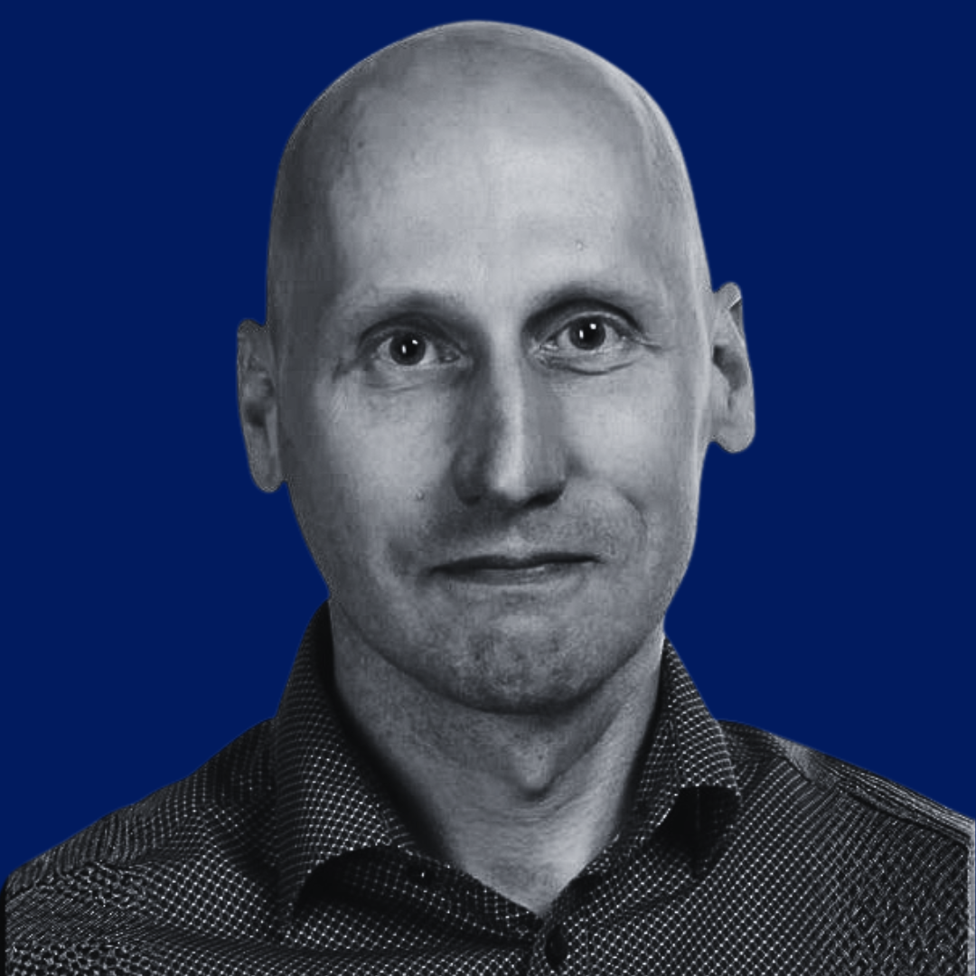 Black and white photo of a bald man in a button-up shirt, set against a dark blue background.