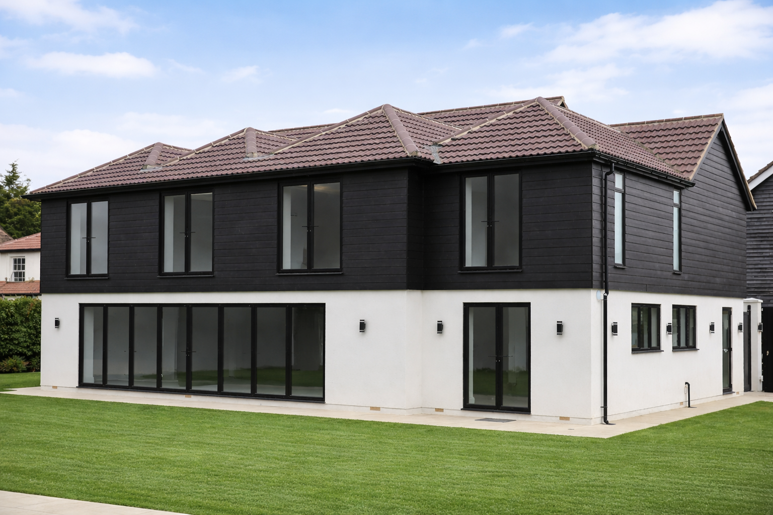 Modern two-story house with black cladding on upper level, white lower level is Silocone rendered, large glass windows, and a well-maintained lawn.