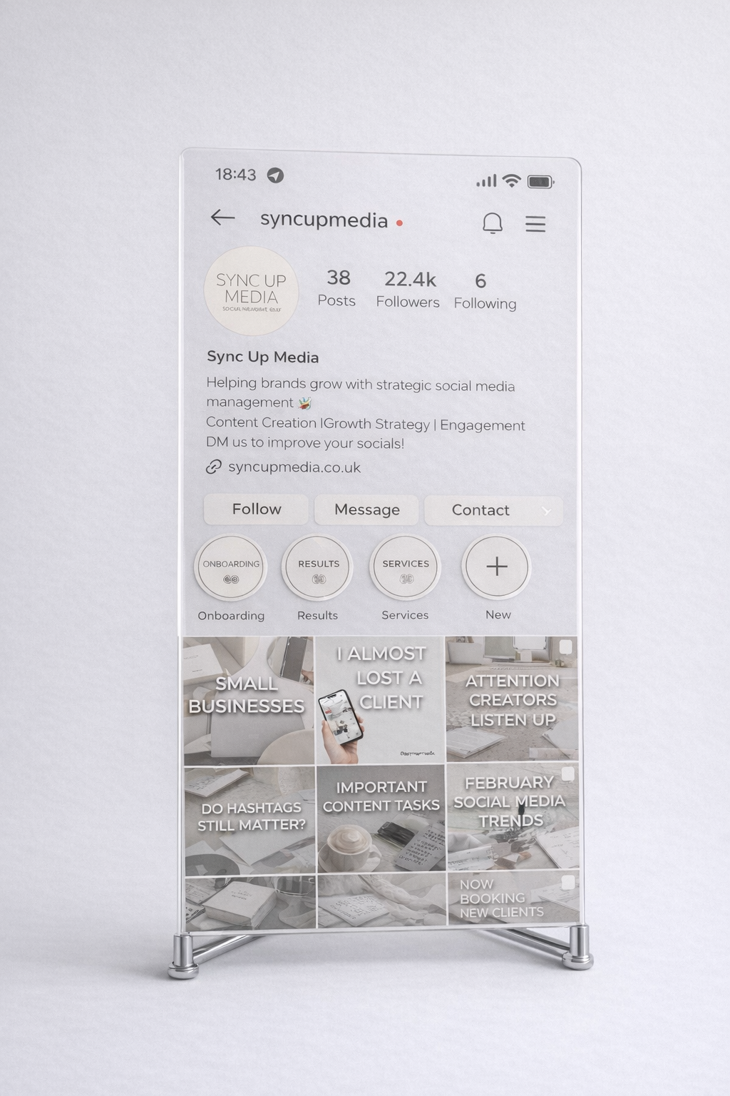 Acrylic display stand showing the Sync Up Media Instagram profile against a soft light grey (#E8E8E8) background.