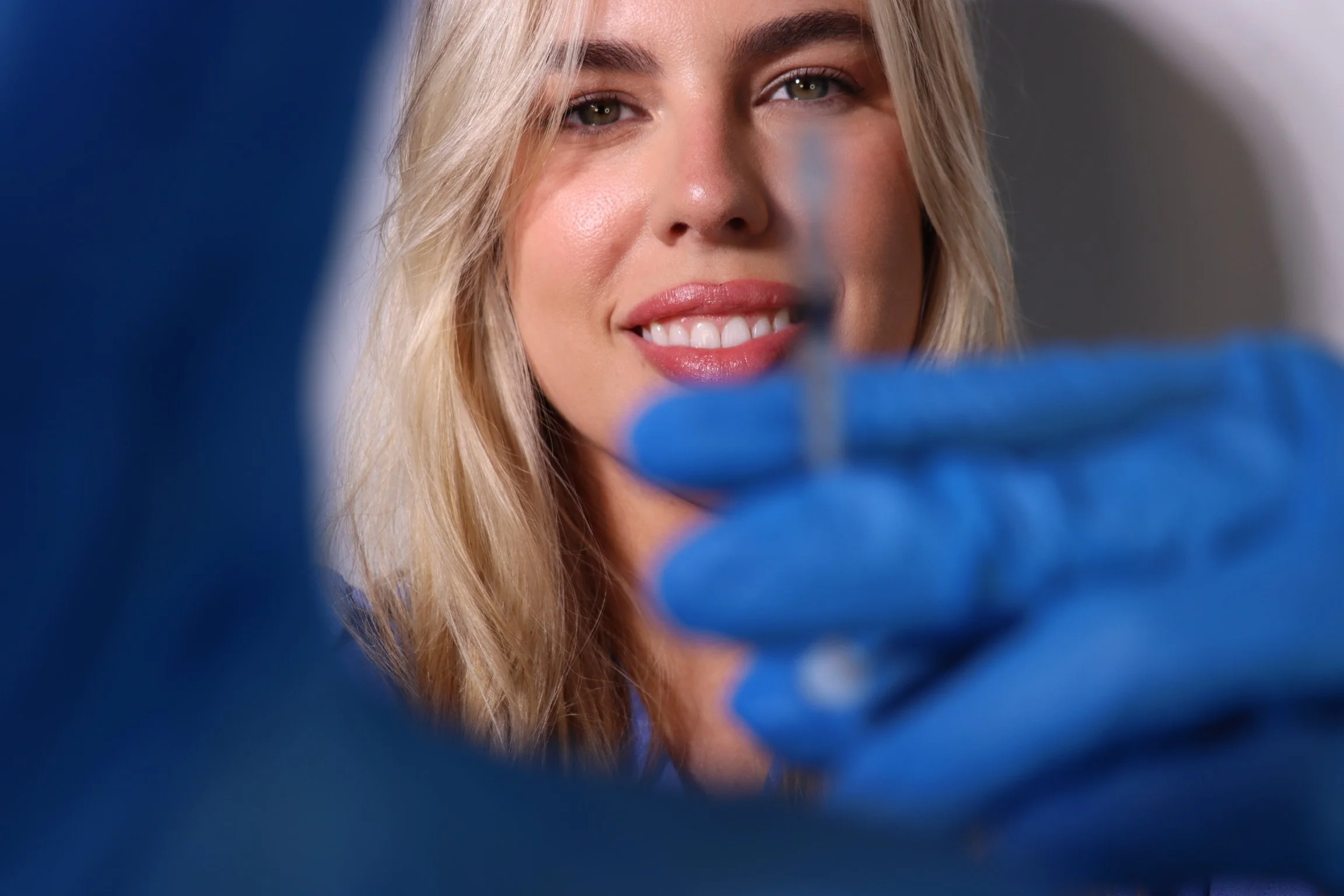 Smiling person in blue gloves holding a syringe