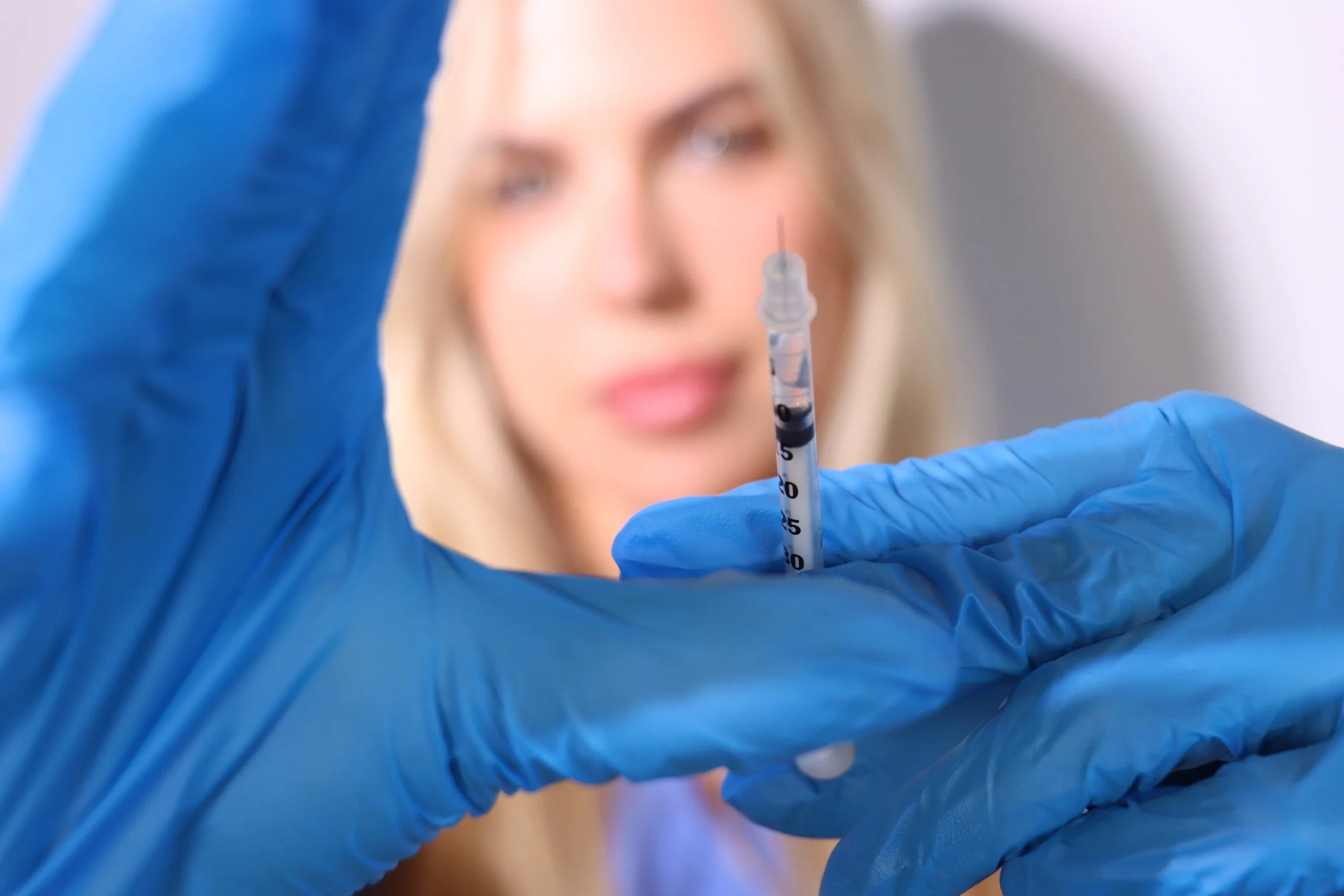 Aesthetic injector holding a syringe in blue gloves, with the focus on the instrument and a blurred background for depth.