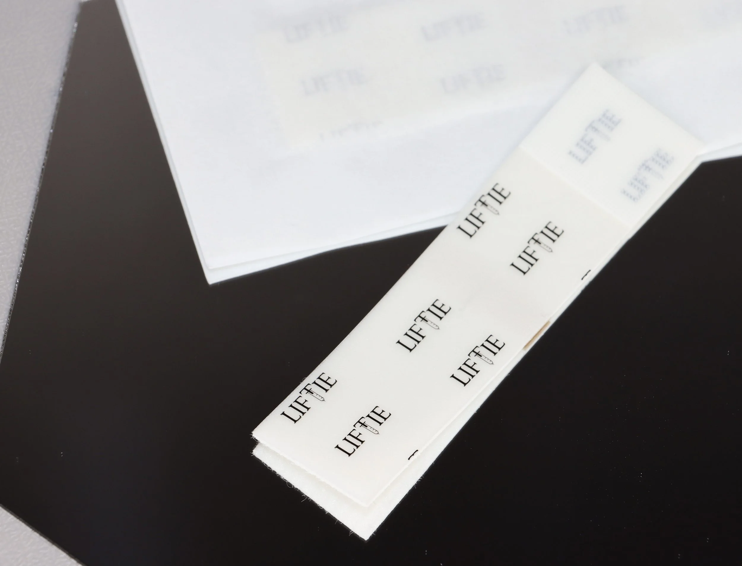 Product detail shot of LIFTIE-branded white adhesive strips laid out on a modern black background.