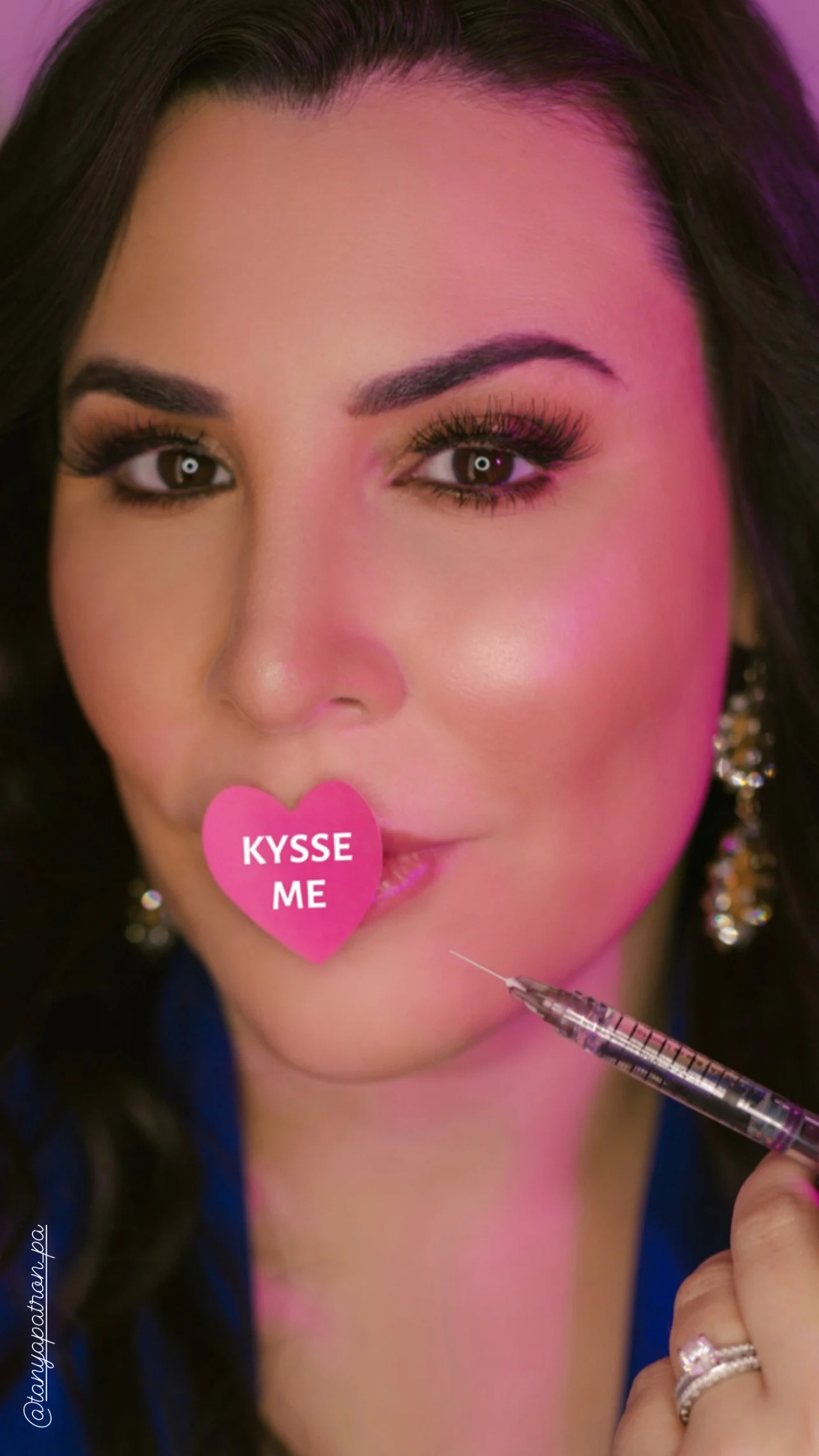 Cosmetic Injector with a pink heart "KYSSE ME" sticker near lips, holding syringe, wearing earrings.