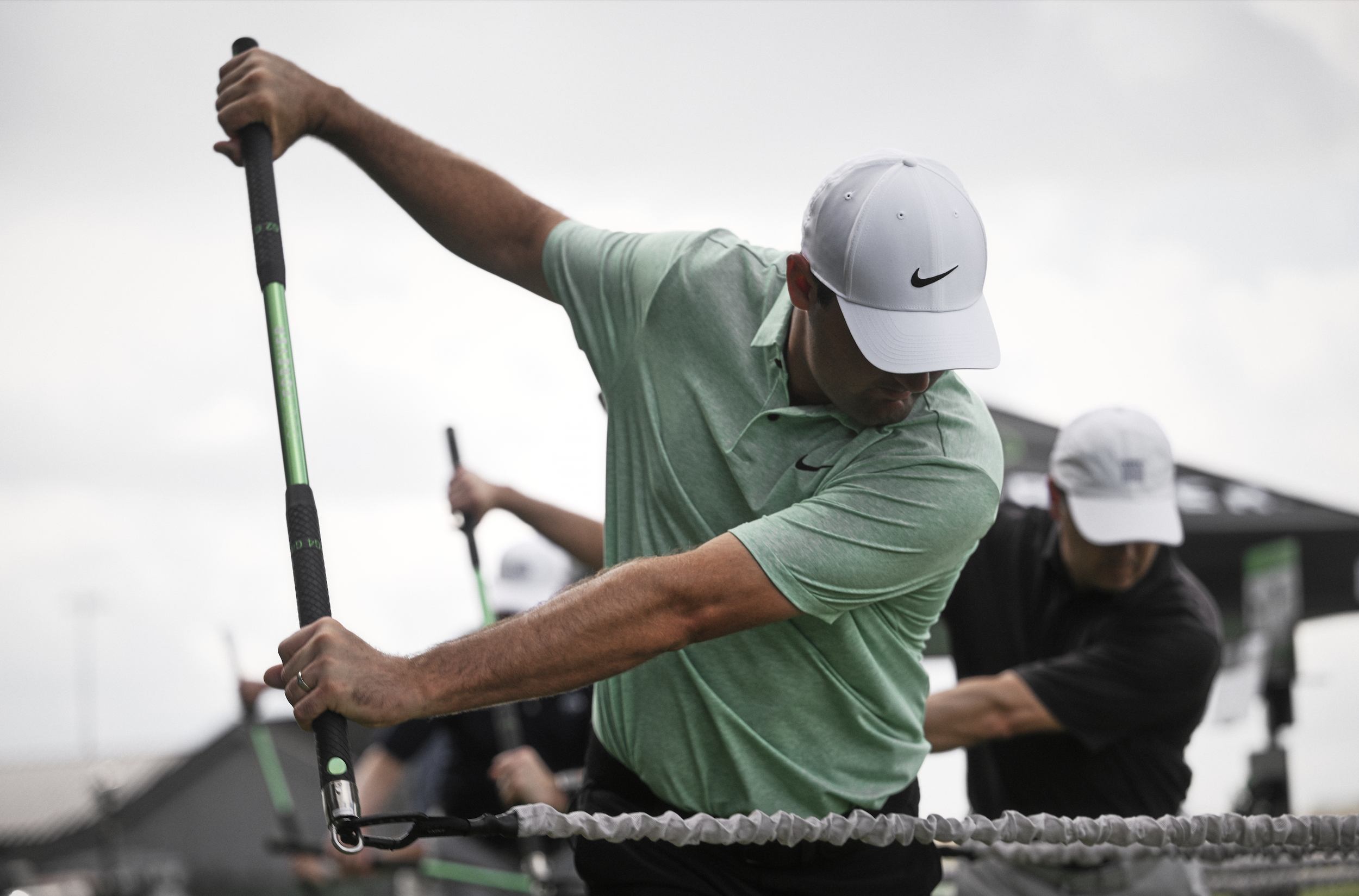 Athletes in white caps and green shirts using exercise bars outside.
