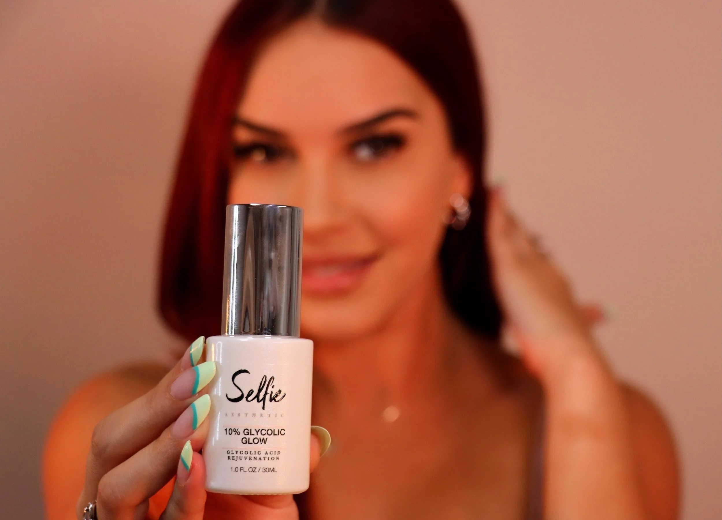 A person holding a bottle labeled "Selfie 10% Glycolic Glow Glycolic Acid Rejuvenation" with colorful nails in focus.