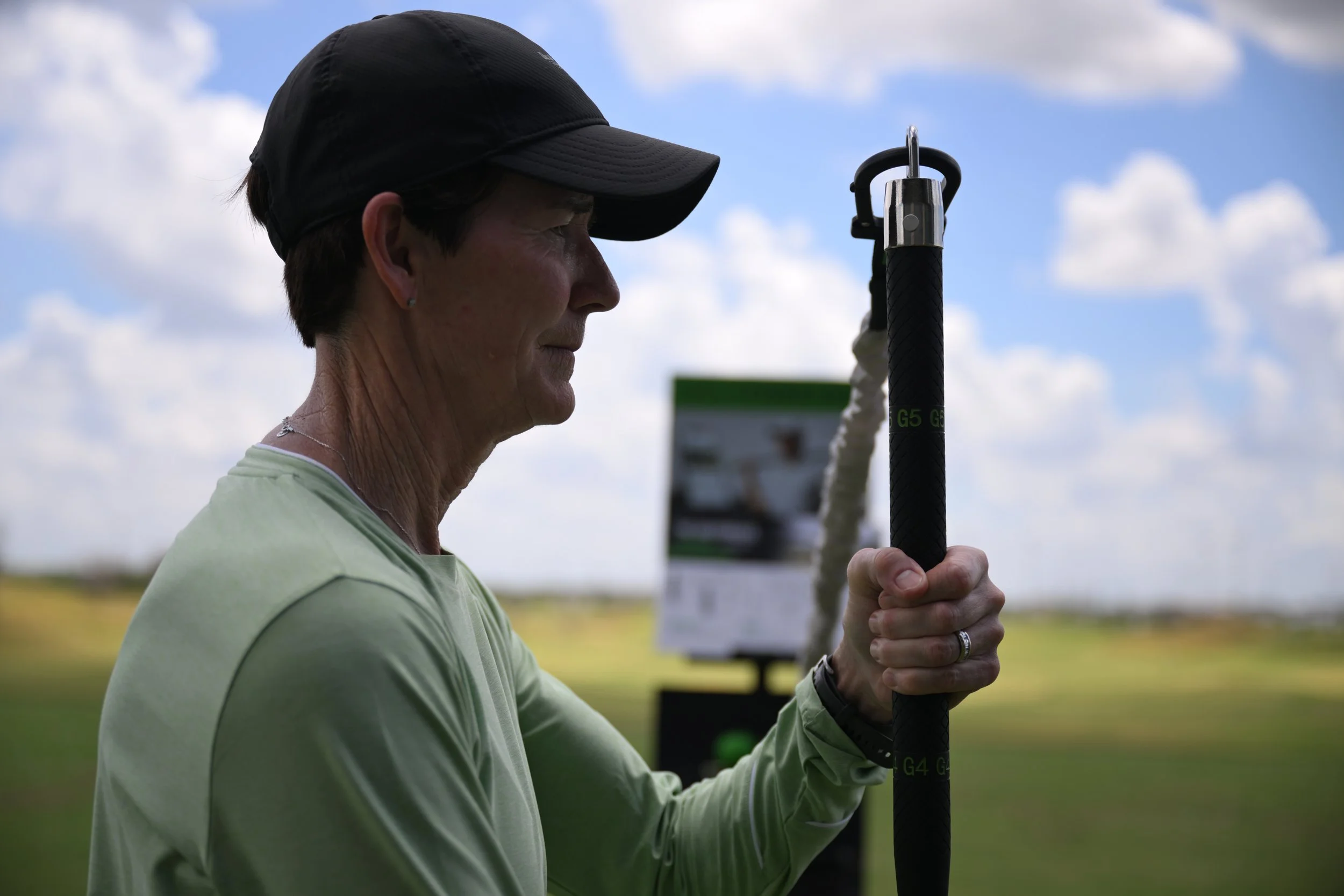 Person wearing a cap holding a long baton-like object outdoors with a cloudy sky background.