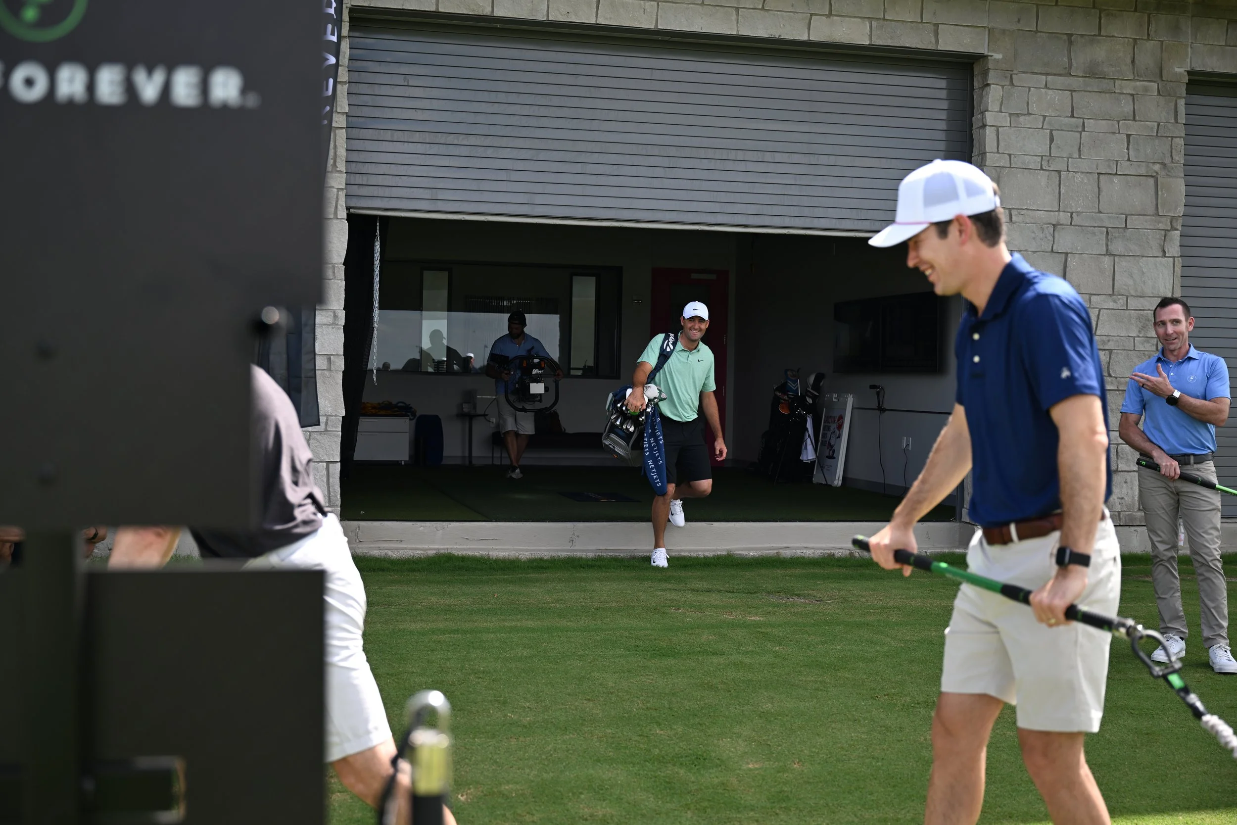 Group of men on a golf course, one carrying a golf bag, others holding equipment, with a building in the background.