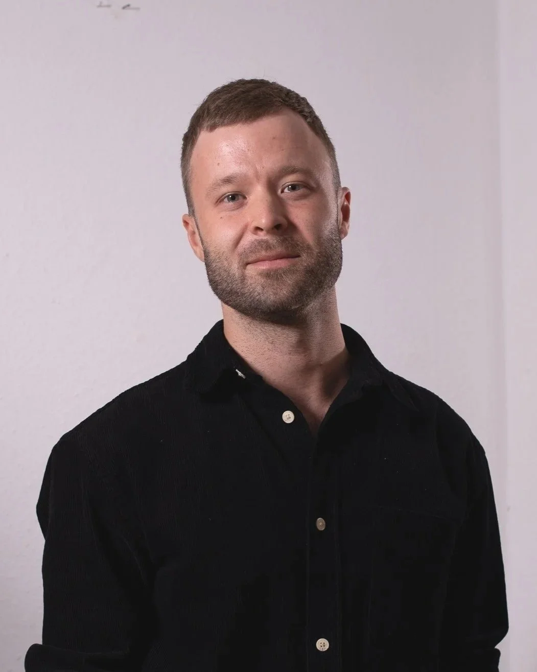 Porträt eines Mannes mit dunklem Hemd vor weißem Hintergrund.