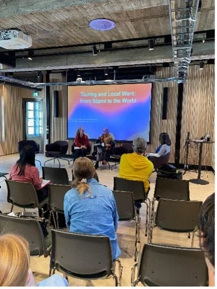 People sit in a conference room where two people are presenting and talking with a presentation screen behind them