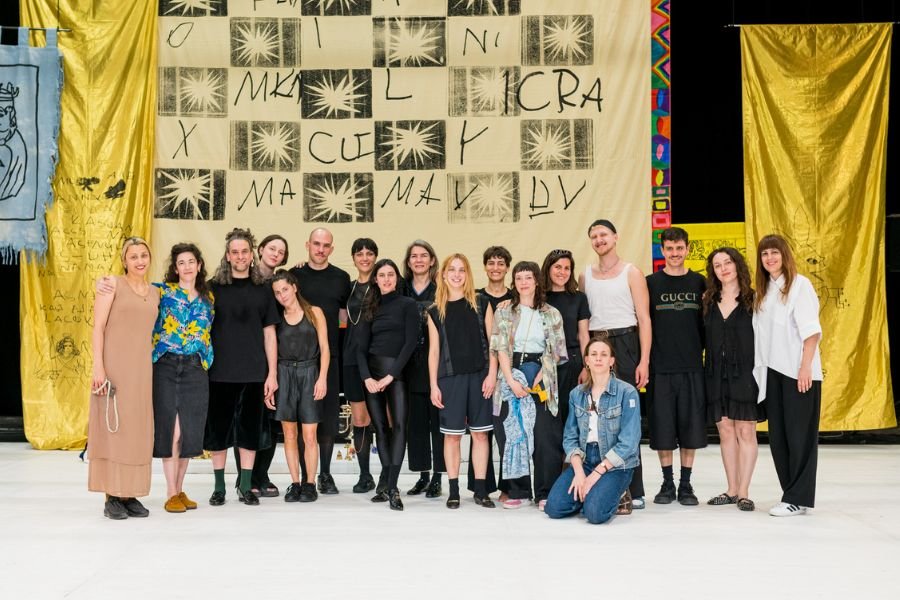 Group of Visiting Artists pose in front of large yellow draping