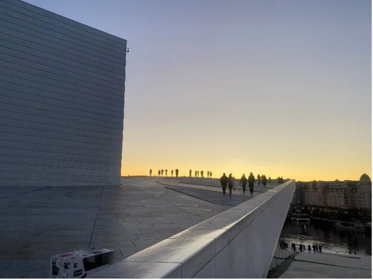 Exterior of a building at sunset with silhouettes of people milling around in the orange light