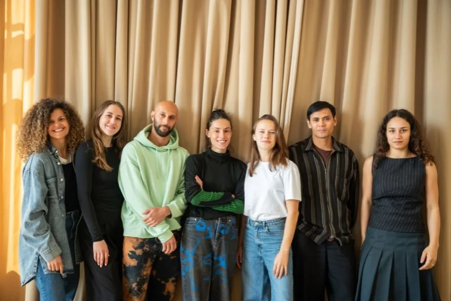 7 people posing together in a line in front of cream coloured curtain