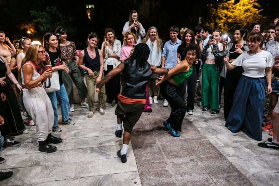 Two dancers swing each other round while a crowd of spectators surround them