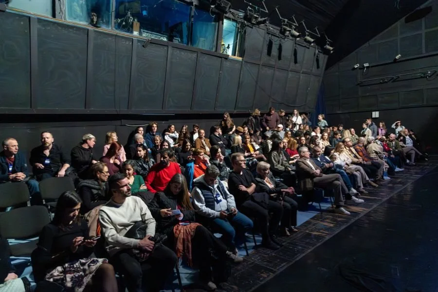 Audience sits in a darkened theatre waiting for the performance to start