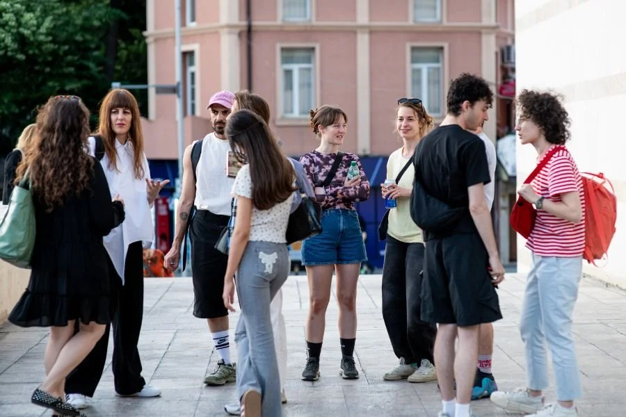 Group of people outside a theatre, stand chatting in small groups