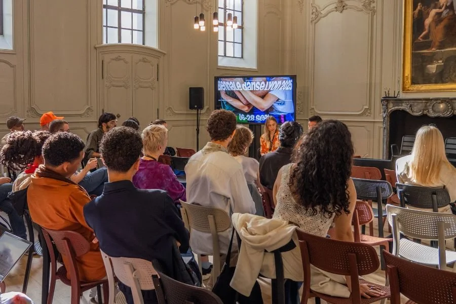 A large room with people seated in auditorium style listening to a presentation
