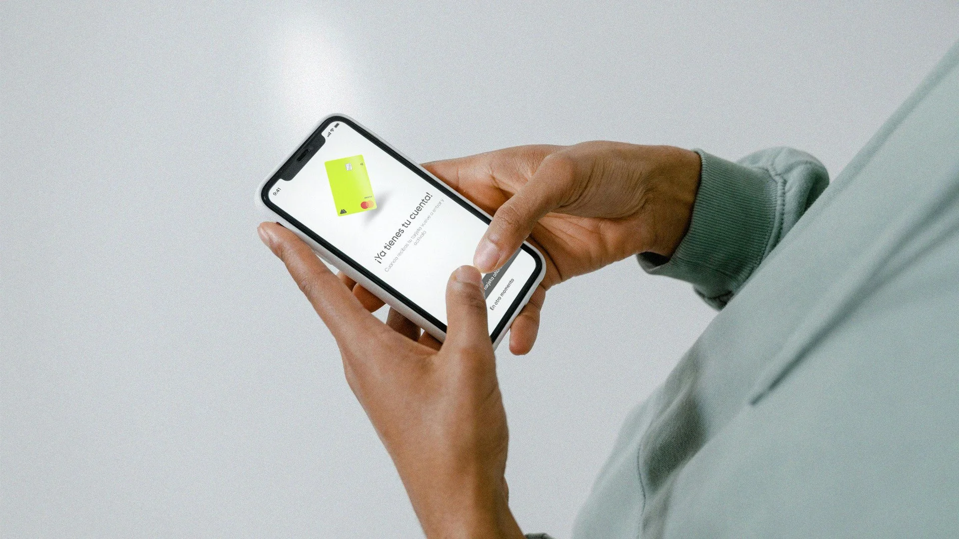 Persona sosteniendo un teléfono inteligente que muestra una aplicación bancaria con una tarjeta verde en la pantalla.