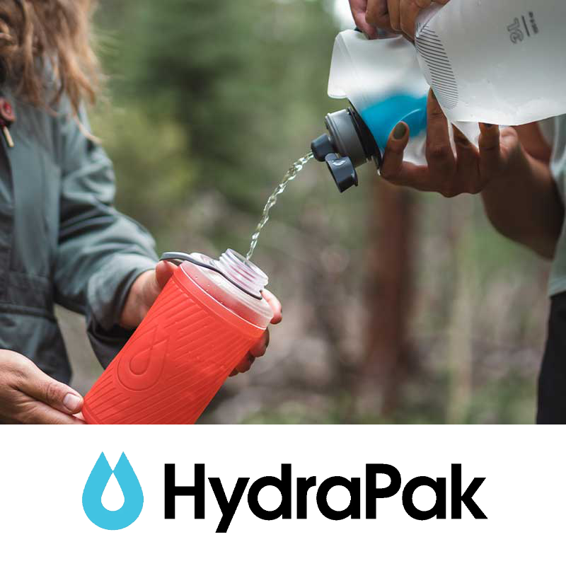 Person pouring water from a hydration bladder into a red insulated water bottle held by another person, outdoors in a forest setting.