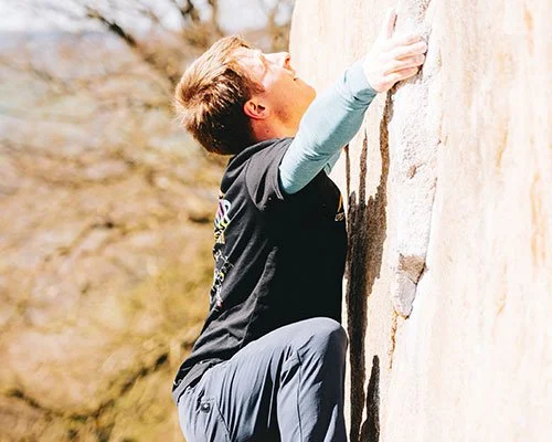 A person climber in a black shirt and gray pants attempting to scale a rock wall outdoors.