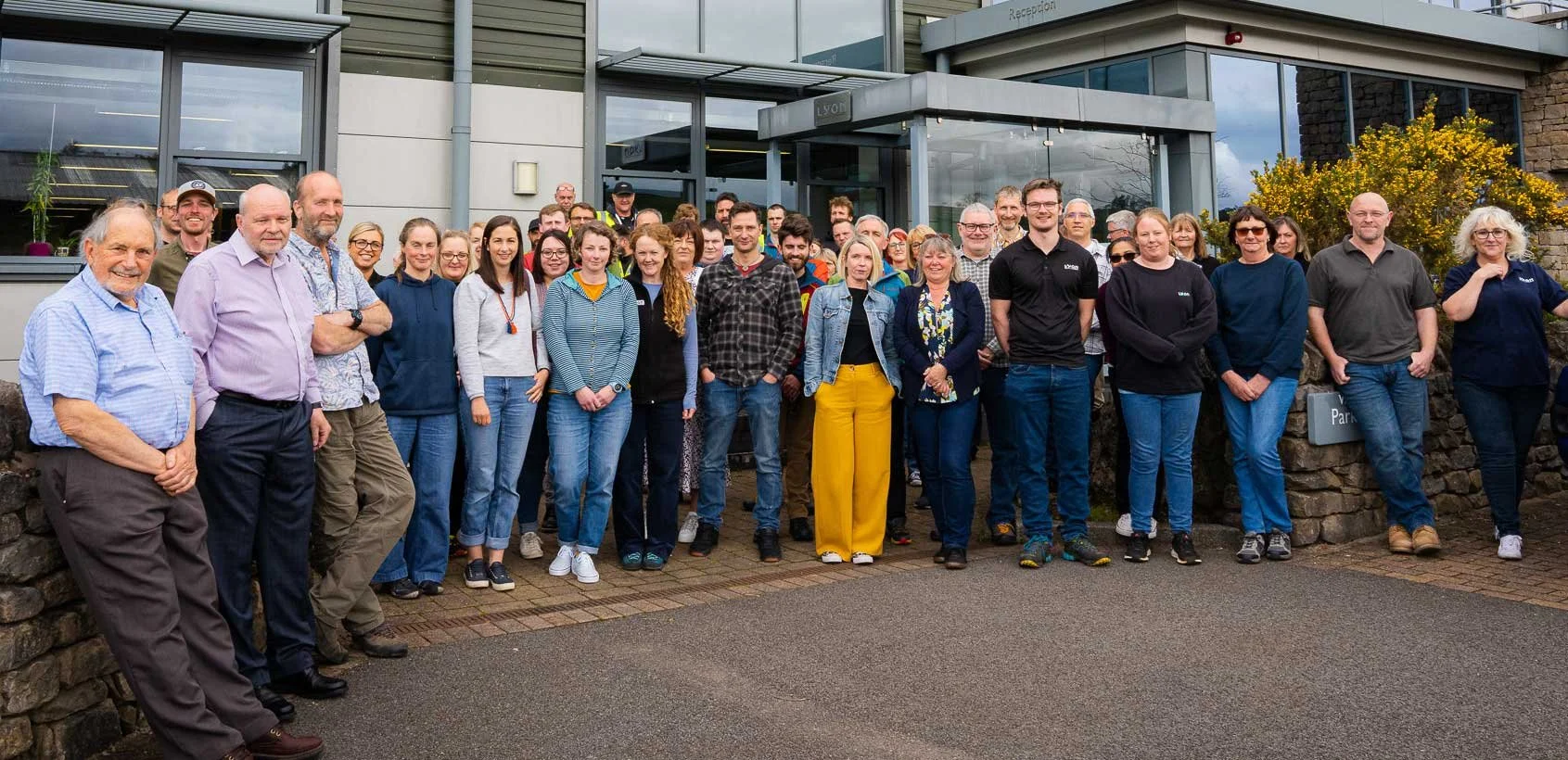Group of people posing outside a building with glass windows and a sign that reads 'Reception'.