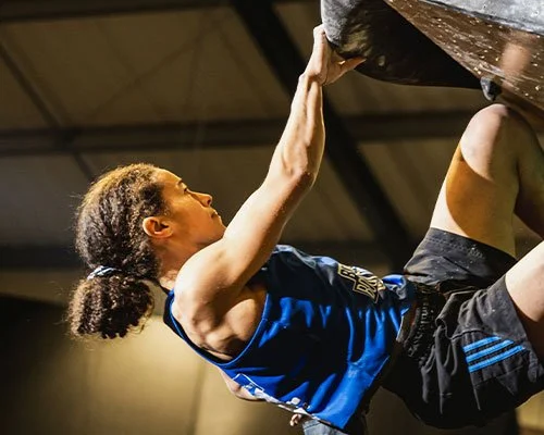 Female athlete climbing a bouldering wall indoors.