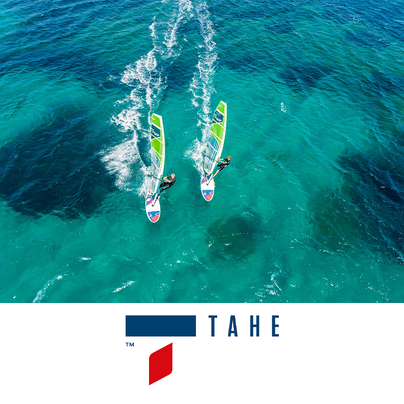 Two people windsurfing on clear, blue ocean water.